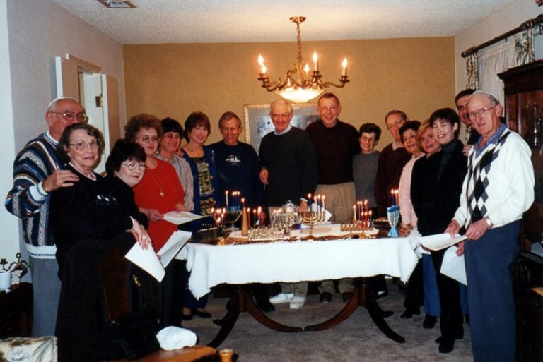 A group of people gathered around a table with lit candles in a cozy dining room, smiling for the camera.