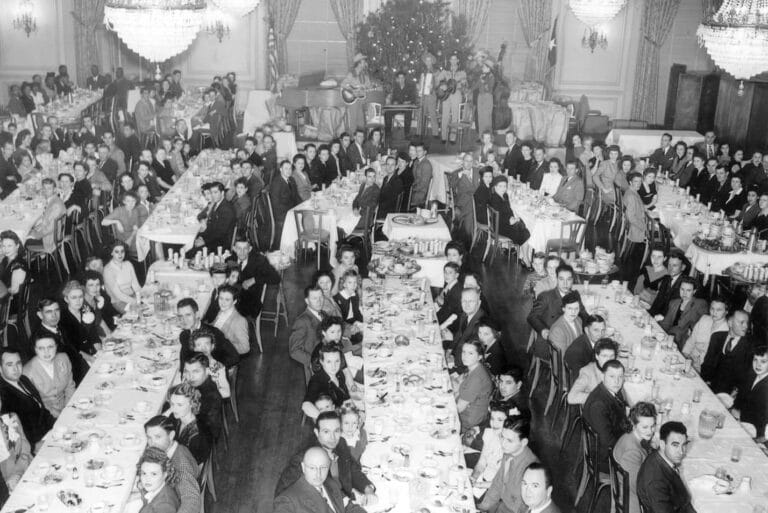 Black-and-white photo of a formal banquet with many people seated at long tables in a decorated hall.