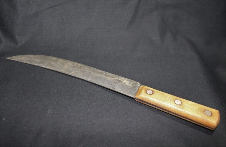 A large, old kitchen knife with a wooden handle and a slightly curved, worn blade on a black background.