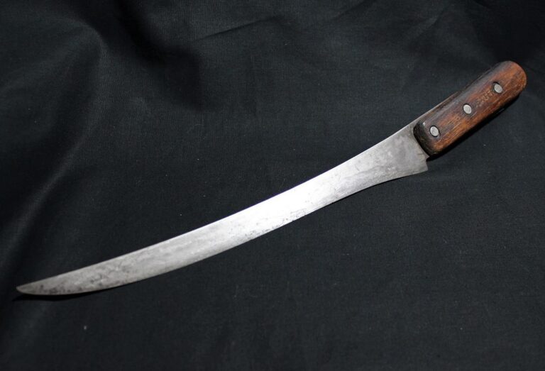 A curved, narrow knife with a wooden handle and three rivets, lying on a black fabric background.