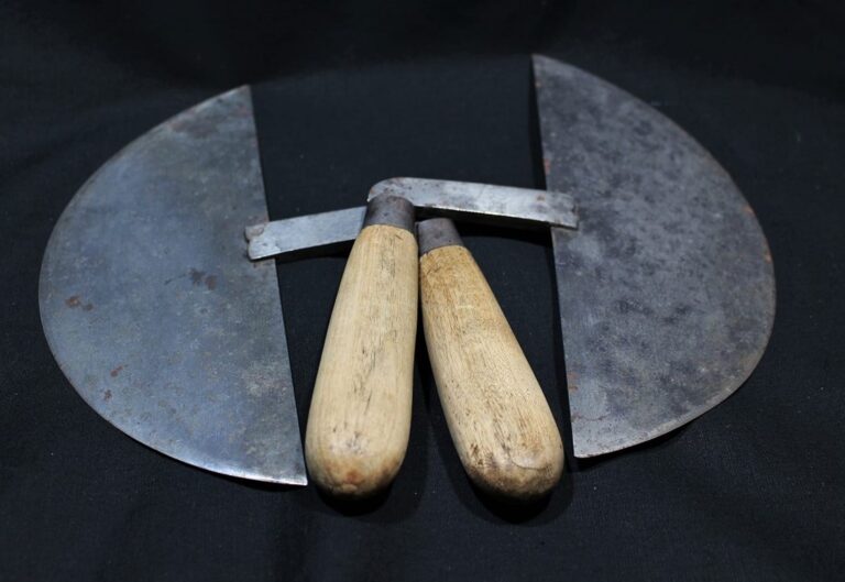 Two mezzaluna knives with wooden handles and curved blades are placed on a black surface.