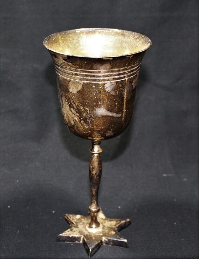 A tarnished, old metal goblet with a star-shaped base, set against a plain black background.