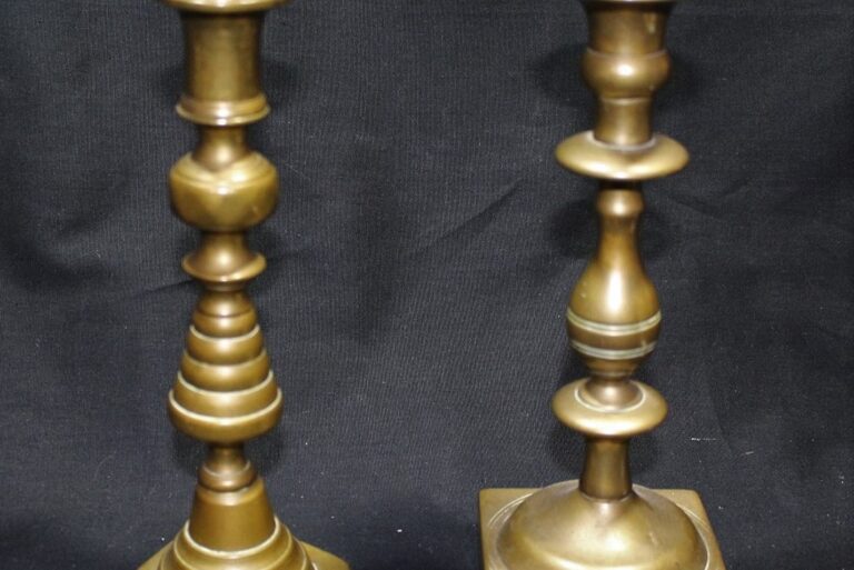 Two brass candlesticks with different designs stand upright against a black background.
