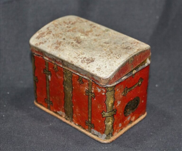 A small, old red metal box with tarnished brass details and a hinged, weathered lid, on a dark surface.