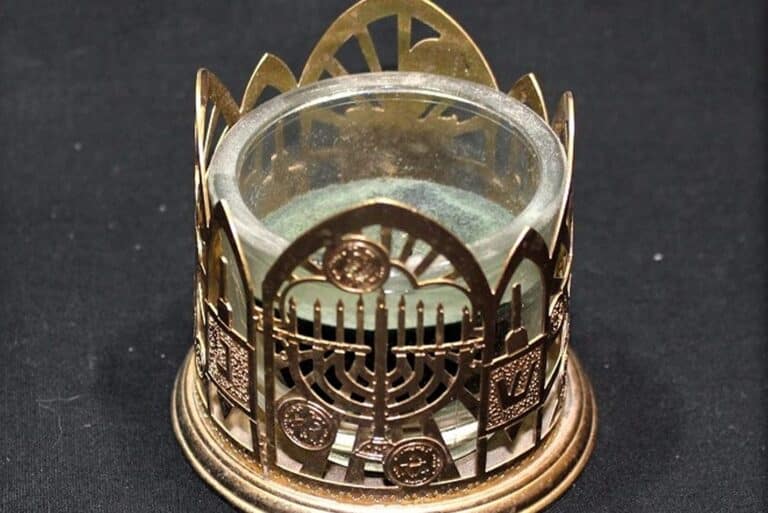 Brass cup holder with an ornate design, including a menorah and Star of David, on a black background.