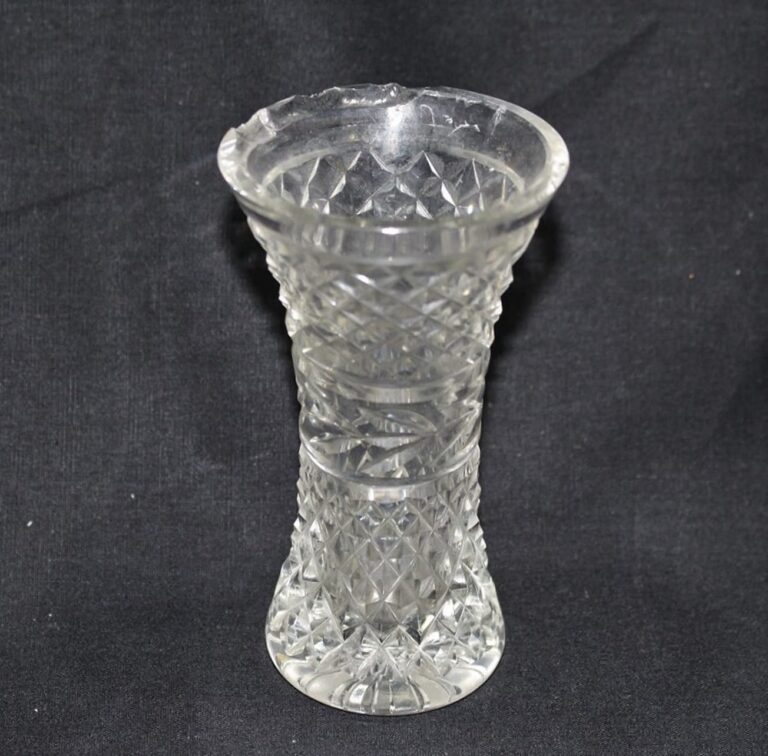 A clear, patterned glass vase with a chipped rim sits on a plain black background.