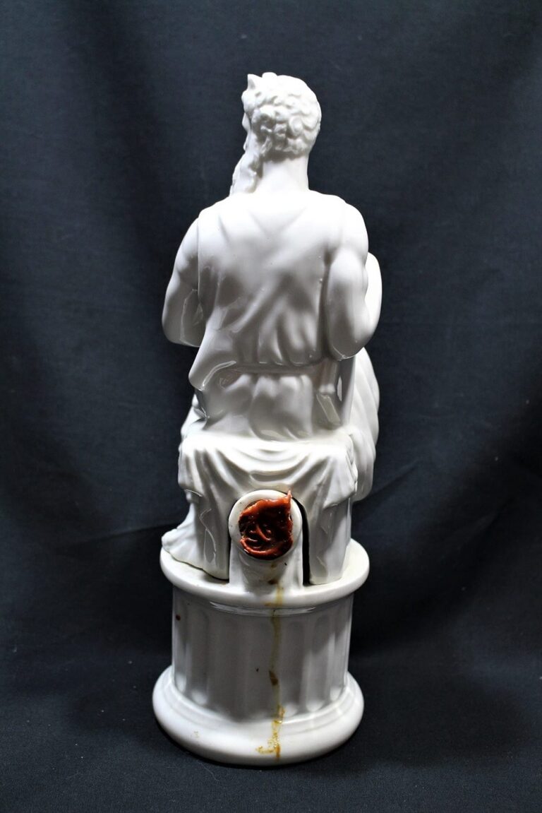 A white porcelain statue of a seated bearded man, viewed from the back, with a visible brown crack near the base.