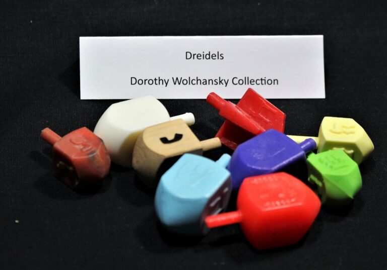Colorful plastic dreidels in front of a label reading “Dreidels, Dorothy Wolchansky Collection” on a black background.