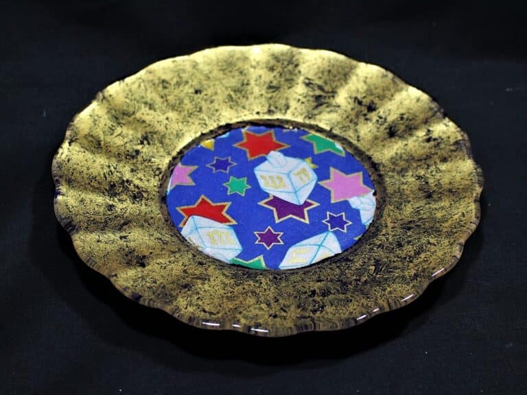 A gold-rimmed plate with a colorful center, featuring stars and geometric shapes on a blue background.