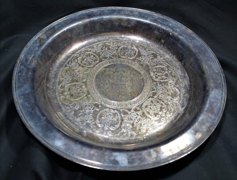 An ornate, round silver platter with intricate engraved patterns, resting on a black cloth background.