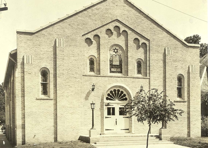 Historic brick synagogue with arched windows, stained glass, double doors, and two lampposts at the entrance.