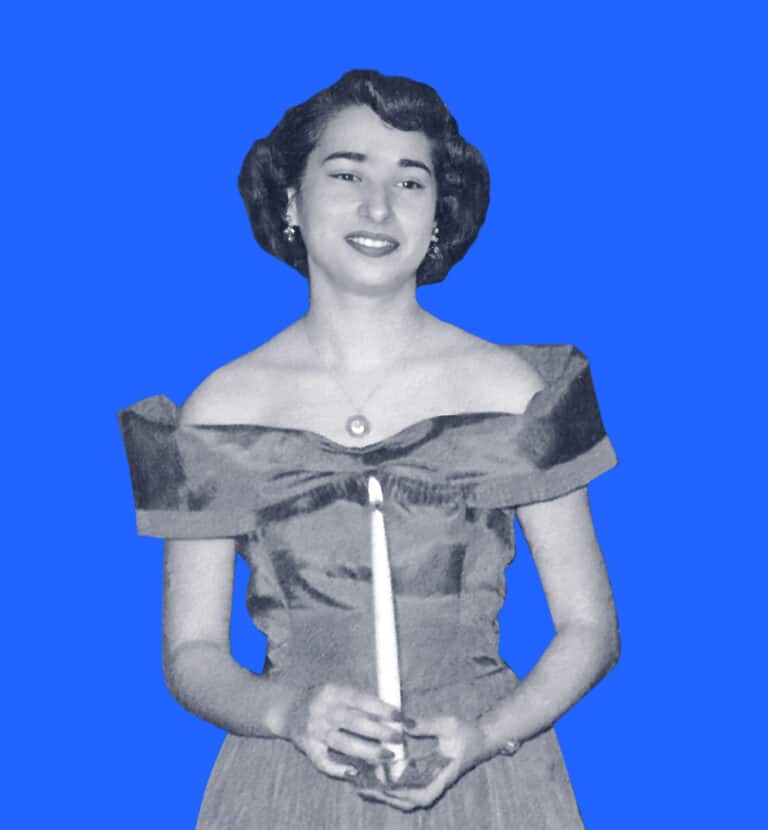 Woman in an off-shoulder dress holds a lit candle, smiling, against a solid bright blue background.