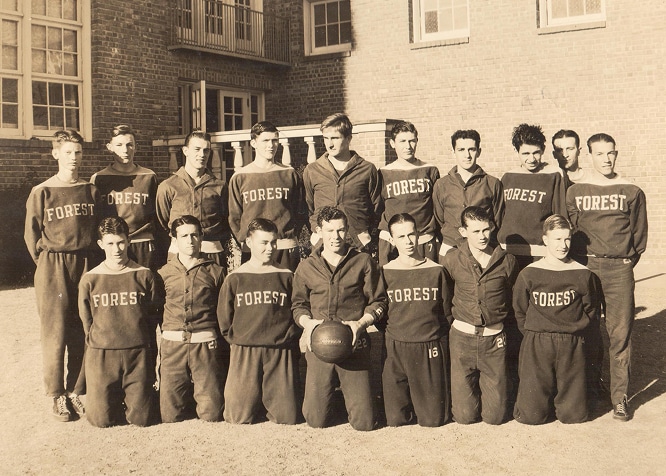 Vintage photo of a basketball team in “Forest” uniforms posing outside a brick building, holding a basketball.
