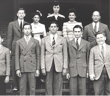 Nine people in formal 1940s attire pose on steps for a black-and-white group photo, four adults and five youths.