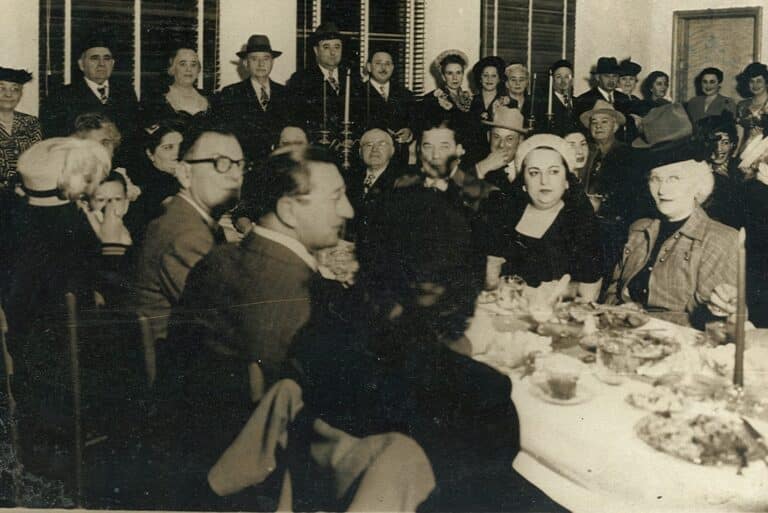 A large group of people dressed formally gather around a table set with food at an indoor event.