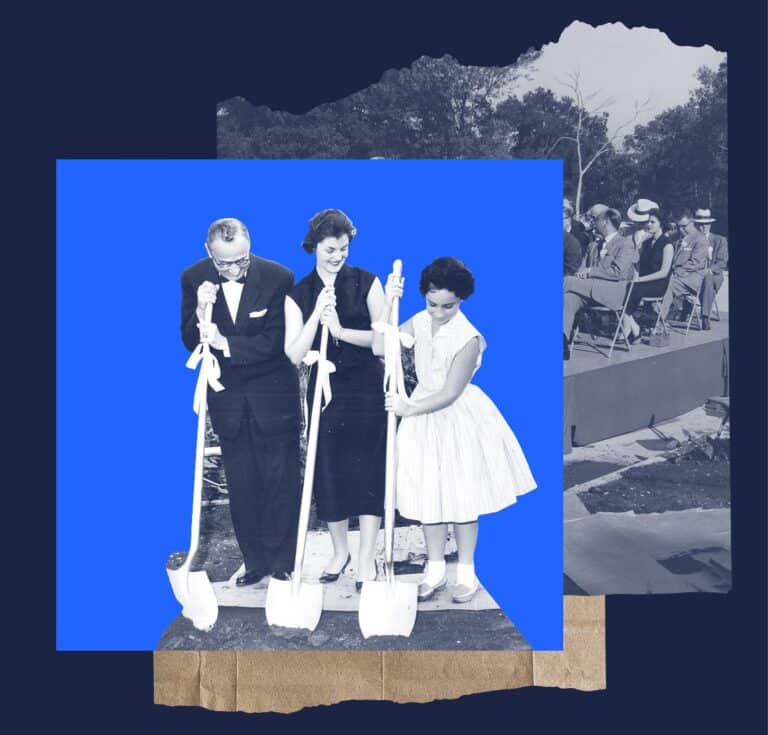 Three people with shovels break ground at a ceremony; an audience sits in the background.