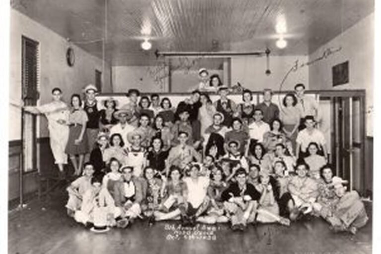 Large group of young people in costumes posing together in a hall, vintage black-and-white photo, circa 1940s.