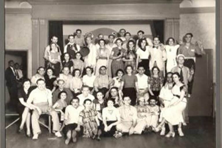 A large group of people pose together in multiple rows on a stage for a black and white photo.
