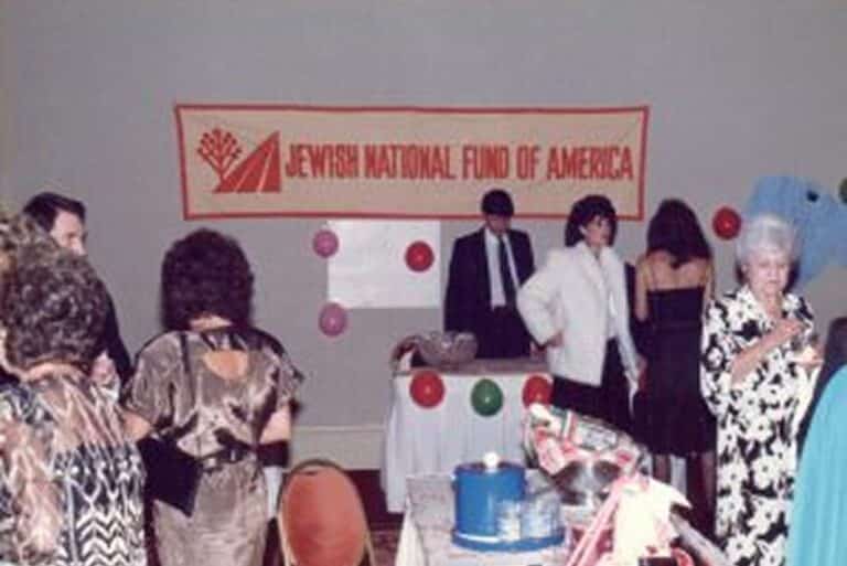 People gather at a Jewish National Fund of America event, with balloons and a decorated table in the foreground.