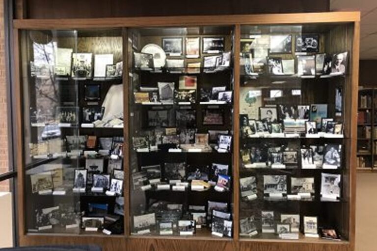 A display case filled with old photographs and documents, arranged on shelves inside a library.