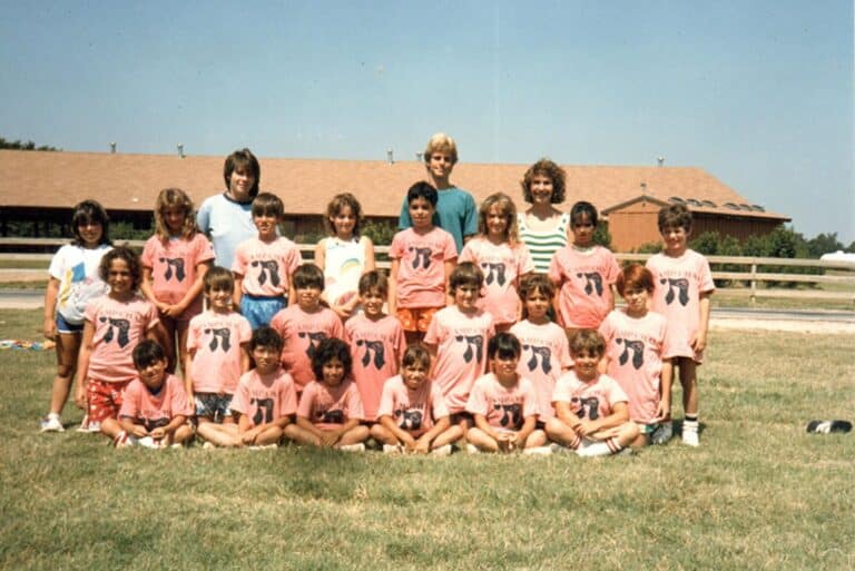 A group of children and two adults in matching pink shirts pose for a group photo outdoors on grass.