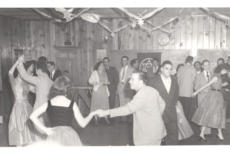 Vintage black-and-white photo of people dancing at a decorated indoor party, wearing 1950s-style formal clothes.