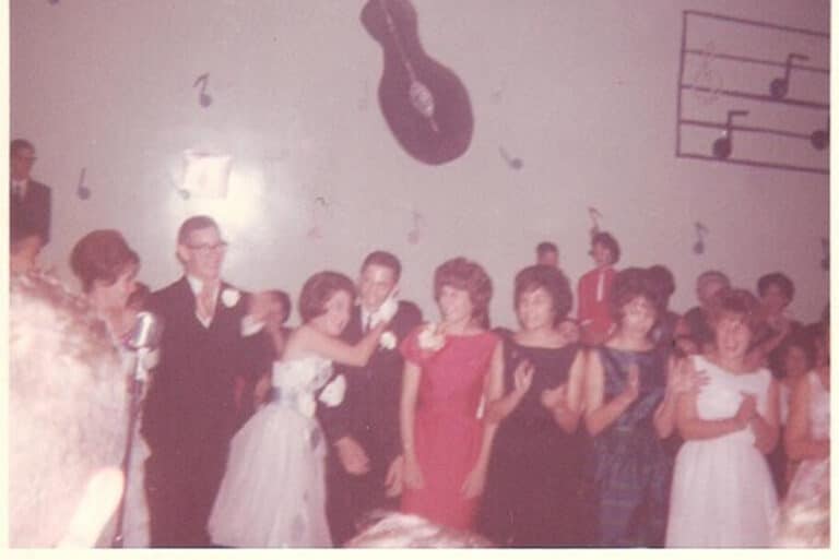 A group of people in formal attire at a dance with music note wall decor and a large guitar decoration behind them.