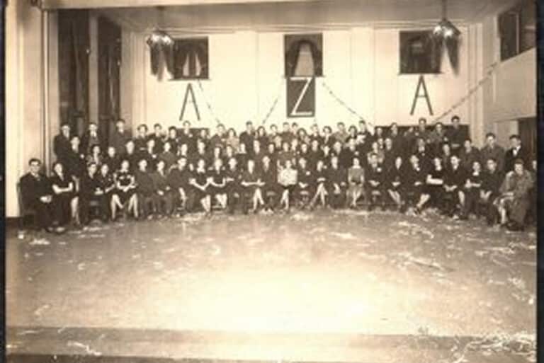Large group of people pose in a hall with “A Z A” letters and streamers on the back wall, early 20th century style.