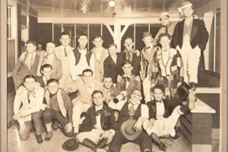 Vintage photo of a group of young men in costumes, posing together indoors in sepia tone.