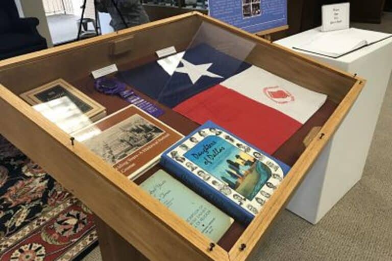 A display case with a Texas flag, books, a blue ribbon, and historical documents inside a museum.