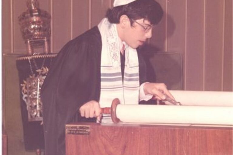 A person in religious attire reads from a Torah scroll in a synagogue.