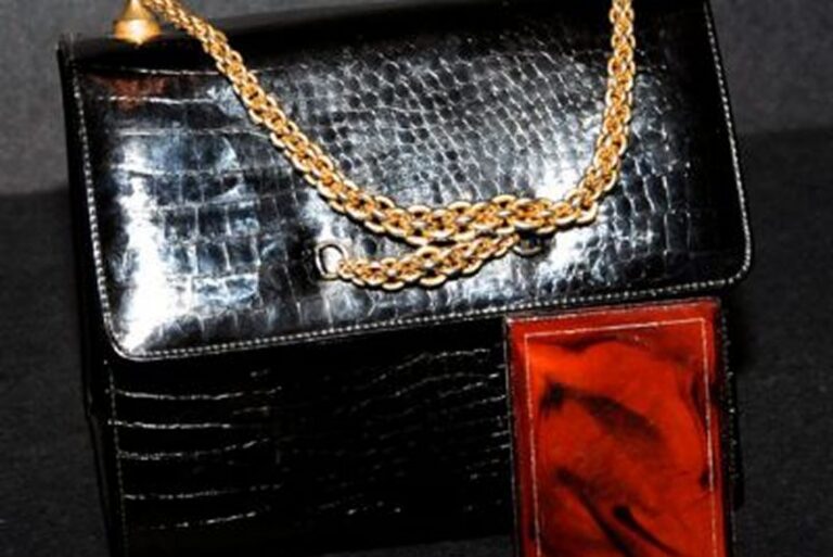 A black crocodile leather handbag with a gold chain strap and a reddish-brown accent on the front.