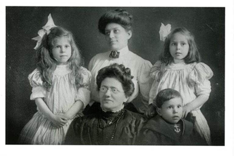 Five people, three women and two children, posing for a formal black and white portrait in old-fashioned clothing.