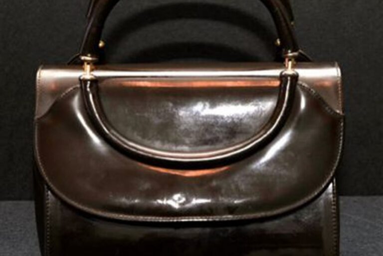 A shiny dark brown leather handbag with a curved flap and two handles, set against a black background.