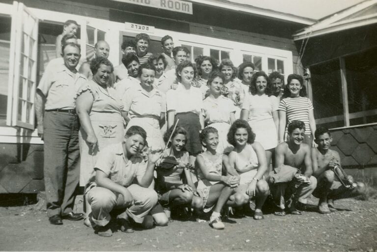 A large group of people posing and smiling in front of a building labeled “Dining Room” in black and white.