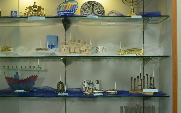 A glass display case with various menorahs, Hanukkah decorations, and festive items arranged on multiple shelves.