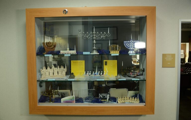 Display case with various menorahs, artifacts, and historical items arranged on three glass shelves.