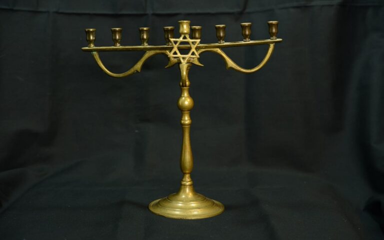 A brass menorah with eight branches and a central stem, featuring a Star of David, on a dark background.
