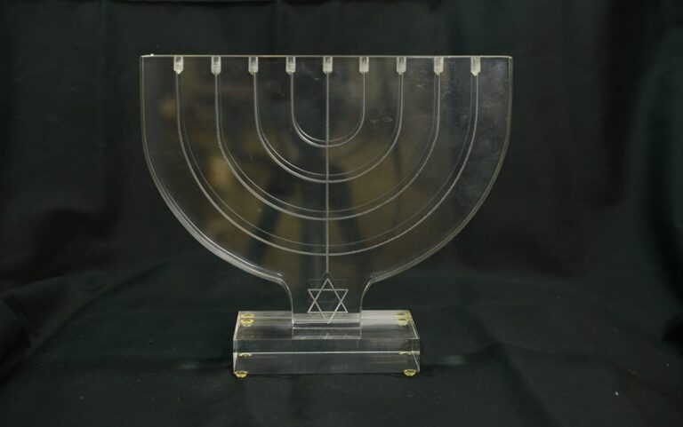 Clear acrylic menorah with a Star of David at the base, displayed on a dark, fabric-covered background.