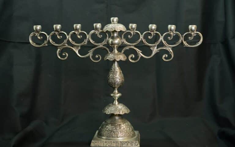 Ornate silver menorah with intricate designs, set against a dark background.