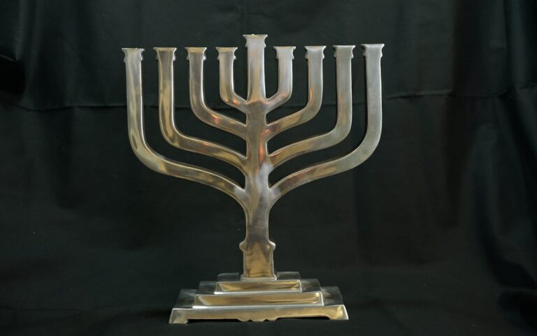 A silver menorah with eight branches and a central holder set against a black background.