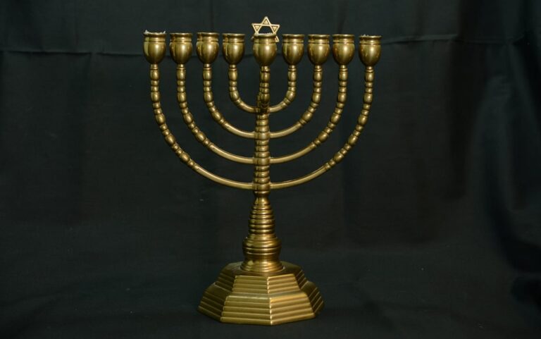A brass menorah with nine branches and a Star of David on top, set against a black background.
