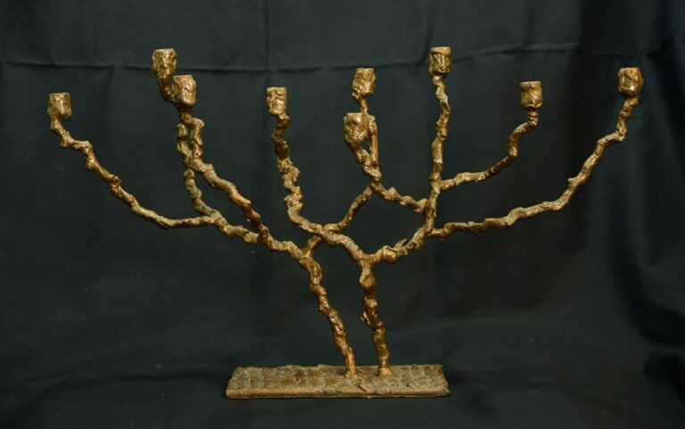 A bronze, tree-like menorah with seven branches, set against a plain black background.