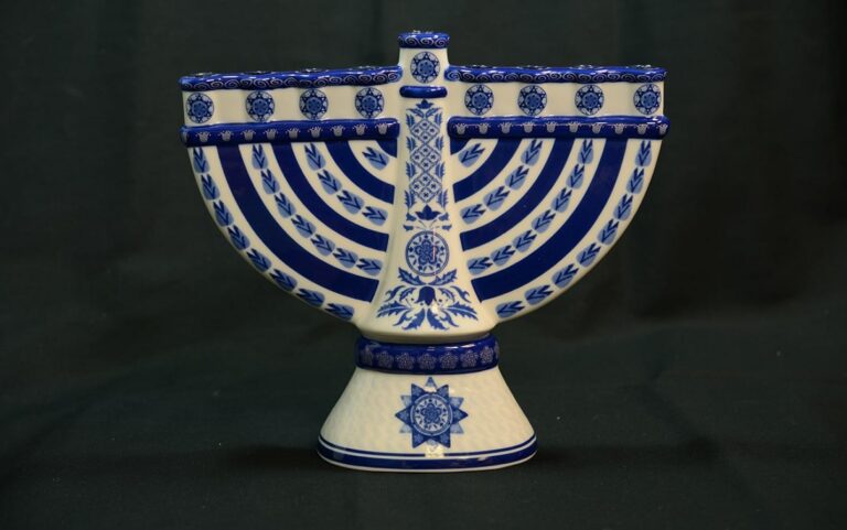 Blue and white ceramic menorah with decorative patterns on a dark background.