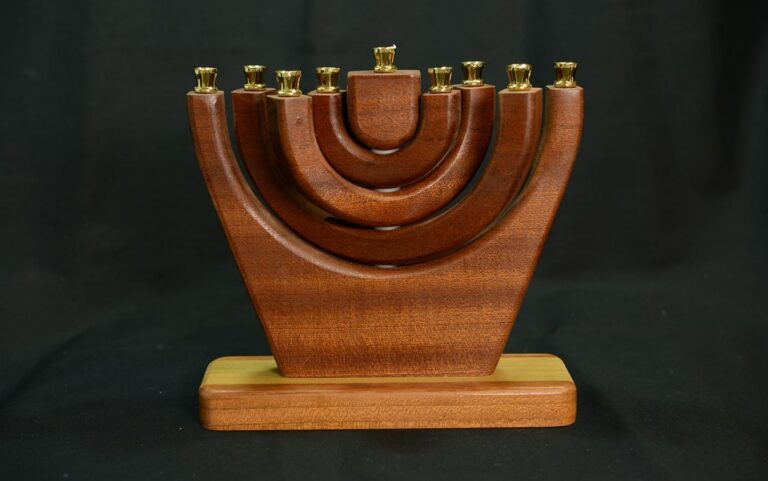 A wooden menorah with gold candle holders, set on a wooden base, against a dark background.