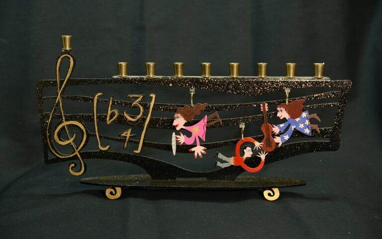 Menorah shaped like musical notes with three playful children figures hanging from it, set against a black background.