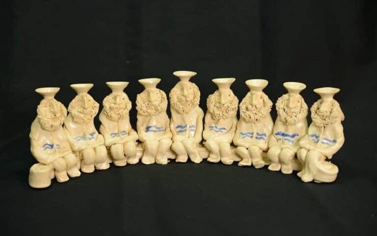 Nine carved ivory figures sitting in a row, each with a wreath and blue markings, on a black background.