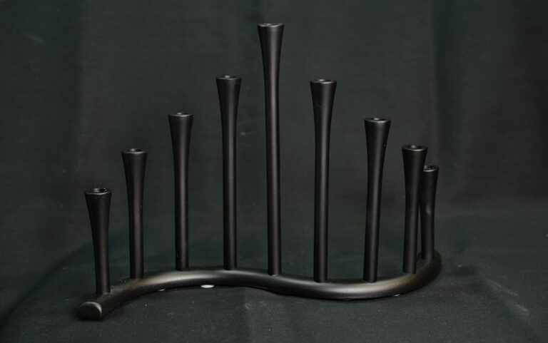 A black metal menorah with a modern, curved design displayed against a dark background.