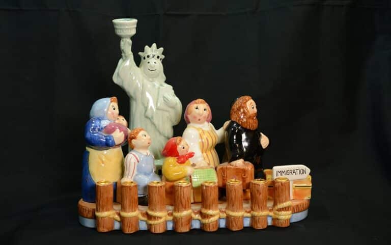 Ceramic figurines of immigrants and Statue of Liberty, with a sign reading “IMMIGRATION,” against a black background.