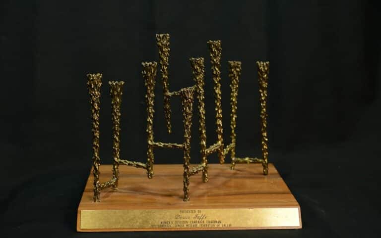 Abstract bronze sculpture with vertical rods on a wooden base, featuring a gold plaque with engraved text on the front.